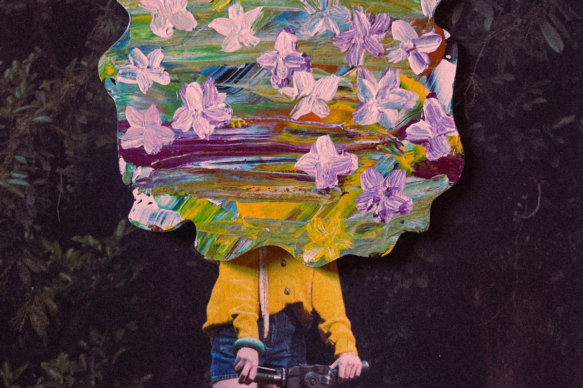 A person in a yellow long-sleeve top and denim shorts stands outdoors holding a yellow pump, with a large abstract floral artwork covering their head. The artwork features pink, purple, green, and yellow brushstrokes, set against a dark forest background.